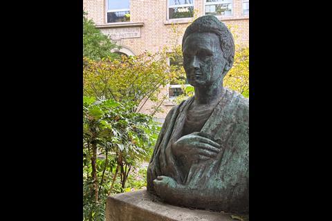 A bronze bust of Marie Curie in a courtyard garden